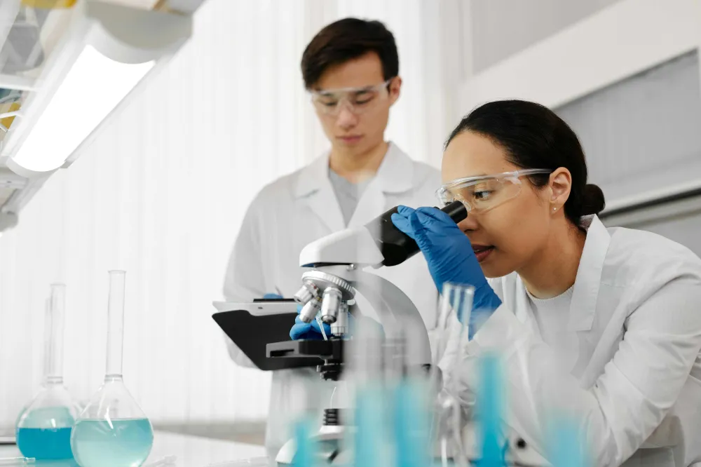 Scientists in a science lab going over a microscope with flasks and bottles around