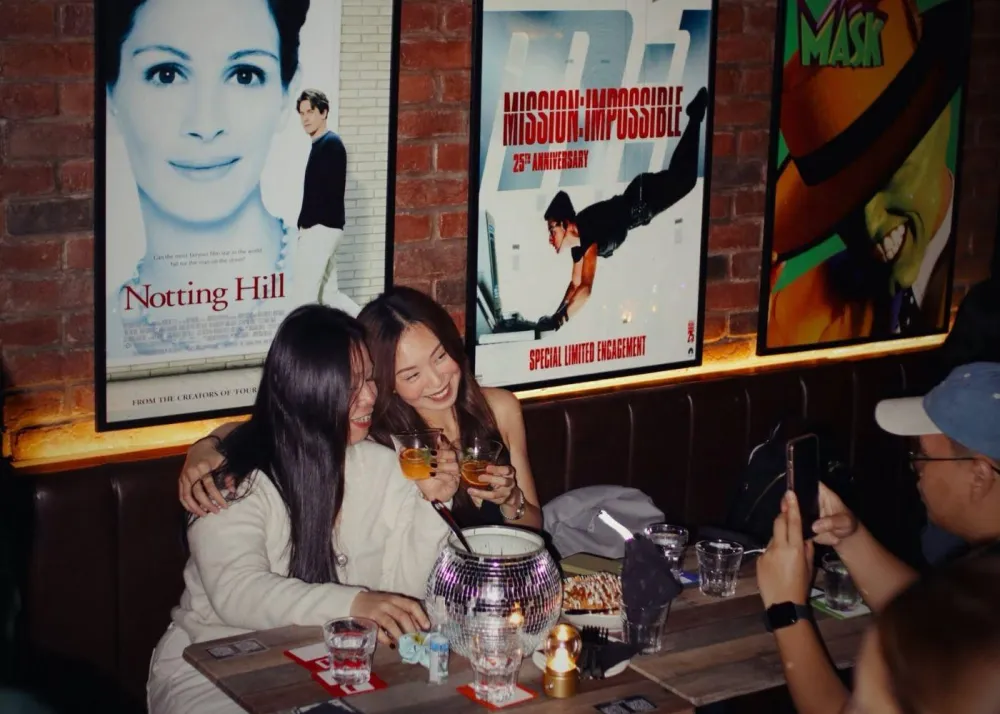 Guests posing to have their photograph taken against a backdrop of old movie posters at Take Me Back speakeasy