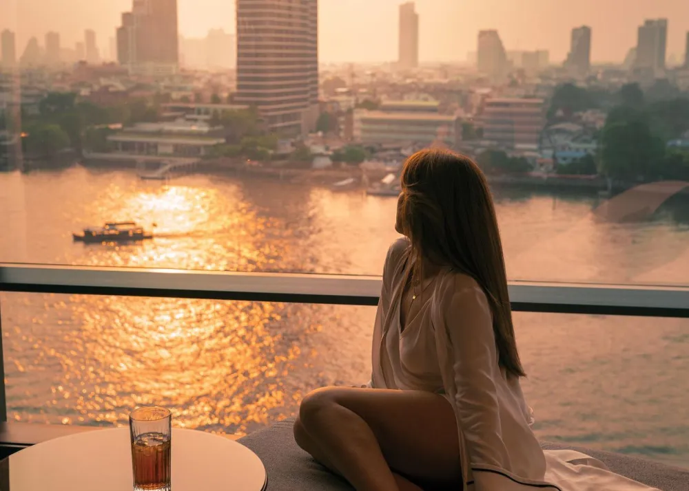 Four Seasons Bangkok at Chao Phraya River woman sitting on balcony overlooking Chao Phraya River at sunset