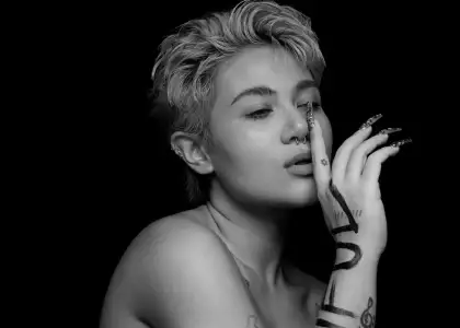 Black and white portrait of SILVY with short hair, a nose ring, and artistic tattoos on hand.