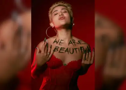 SILVY with short blonde hair, eyes closed, wearing statement earrings and a red lace top. "We Are Beautiful" is written on their chest.