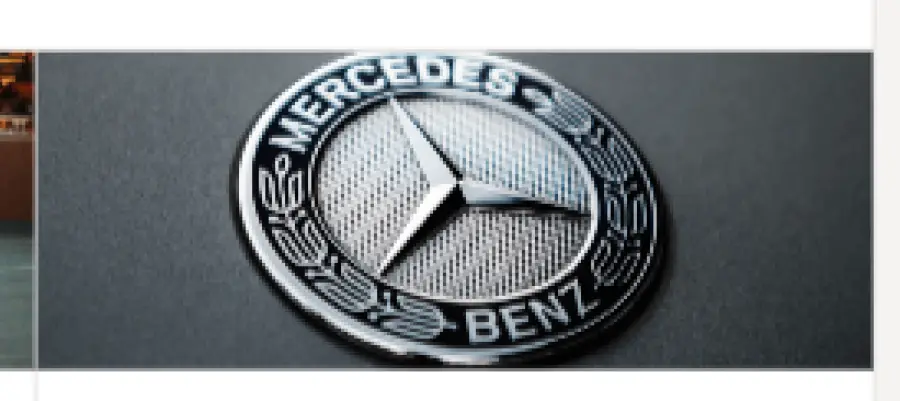Close-up of a Mercedes-Benz emblem featuring a silver three-pointed star encircled by the brand name on a textured background.
