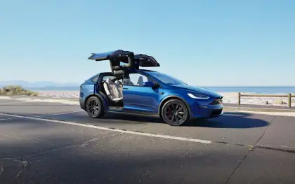 A blue Tesla Model X Plaid with its doors open by the road