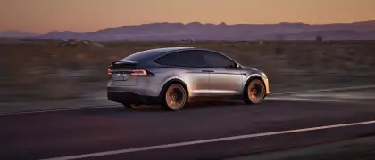 A gray Tesla Model X driving in the sunset