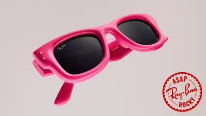 Pink sunglasses, folded, against a neutral background