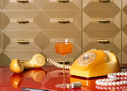 A cocktail with a vintage phone and pearls in the background