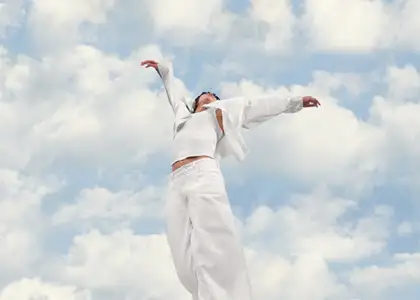 A man with his arms stretched out against a backdrop of clouds