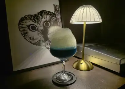 A blue-colored cocktail with an owl photo and lamp