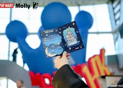 A hand holding the stamp collection postcard and the Giant MOLLY's crown installation at the back