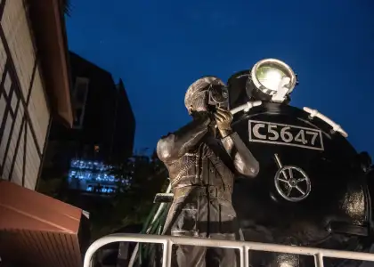 A statue of a train master with a vintage train at the backgound