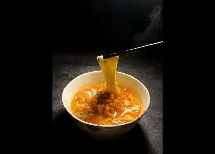 A bowl of soup filled with noodles and pieces of meat, garnished with herbs.