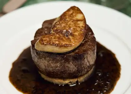 A perfectly cooked steak on a white plate, garnished with a rich sauce drizzled around it.