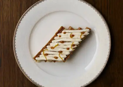 A slice of cake on a white plate, showcasing layers and frosting, set against a neutral background.