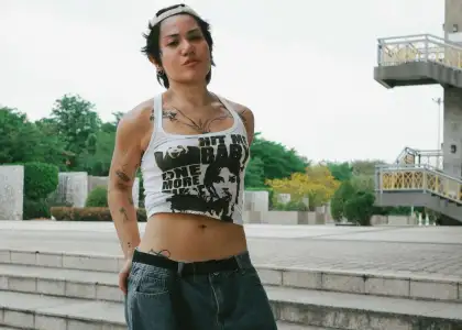 SILVY with short hair and tattoos, wearing a tank top, standing casually on steps outdoors.