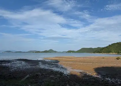 photo of beach against blue sky with mountains in background at Cheung Chau island view from Saiyuen Camping Adventure