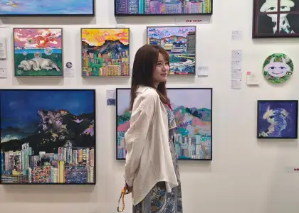 Hong Kong artist Zue Chan smiling and posing in front of her paintings at art exhibition