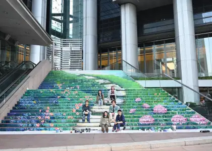 Zue Chan posed with fellow artists sitting on green staircase nature mural