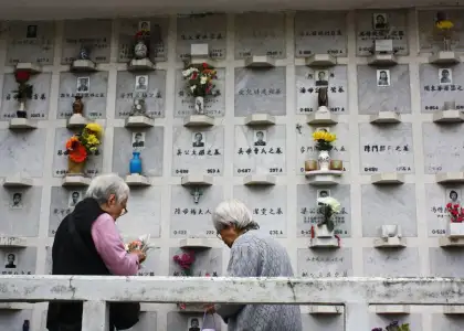an elderly couple standing in front of tombstones with flowers