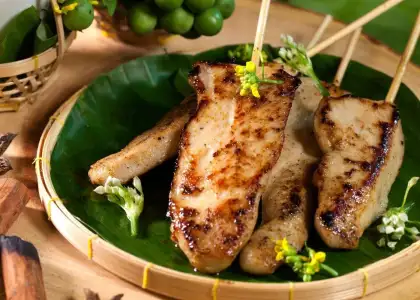 Grilled skewered meat on a banana leaf-lined bamboo plate