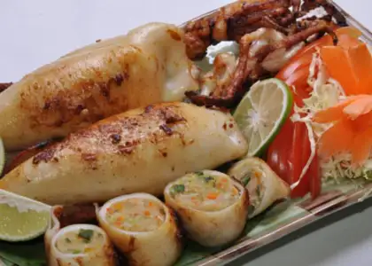 Grilled stuffed squid on a plate with lime slices, shredded cabbage, and sliced carrots