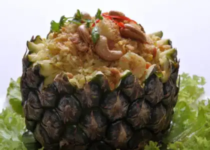 Pineapple rice served in a hollowed pineapple, topped with cashews, shrimp, and herbs, garnished with lettuce