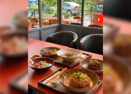 A cozy indoor table with bowls of Asian cuisine, including noodles and soup, on a wooden tray