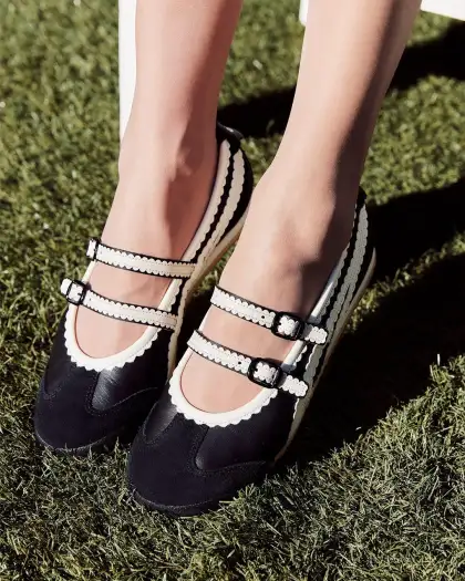 A woman's feet in black and white shoes on bright green grass, showcasing Onitsuka Tiger Ballerina style.