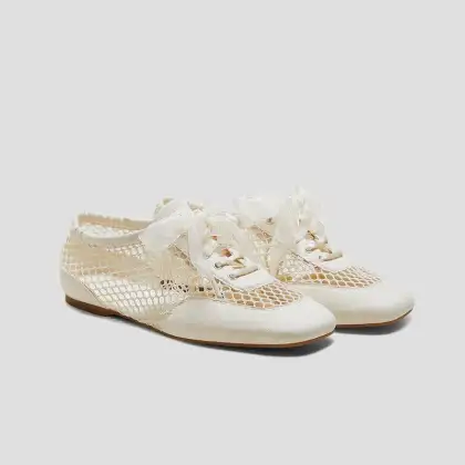 A pair of white lace-up Vivaia Ballerina shoes featuring a decorative bow on each shoe.
