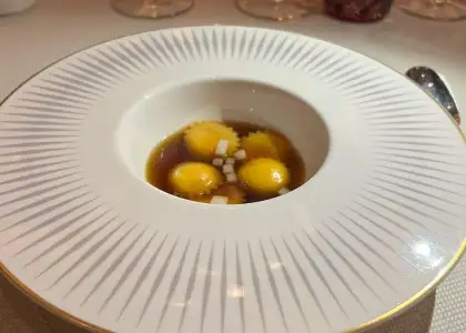 A white bowl of onion soup with ravioli