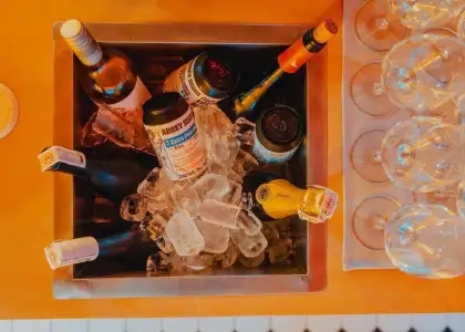 A metal ice bucket filled with various bottles, including wine and beer cans, surrounded by ice cubes.