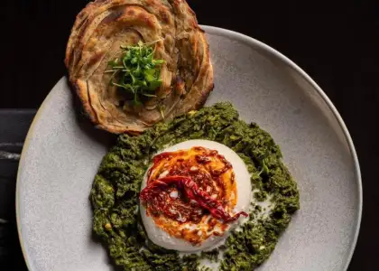 A plate contains a serving of vibrant green spinach puree, topped with a soft, white poached egg and garnished with a drizzle of red chili oil and dried red chilies