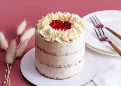 Tall red velvet cake with white frosting and crumb topping, placed on a pink surface