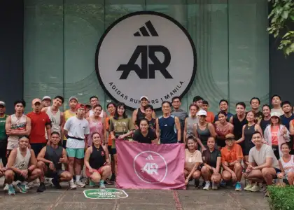A diverse group of smiling runners pose in front of a large "Adidas Runners Manila" sign
