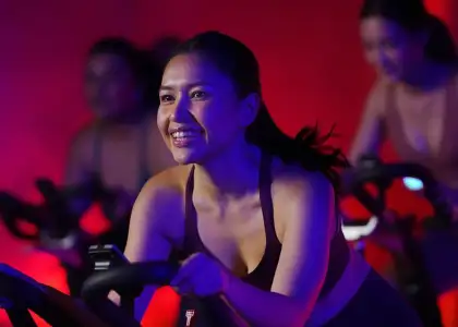 Smiling woman in a dimly lit fitness class rides a stationary bike