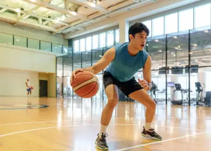 A person in a blue tank top dribbles a basketball on an indoor court