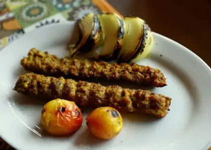 Grilled kebabs with charred onion slices and roasted tomatoes on a white plate