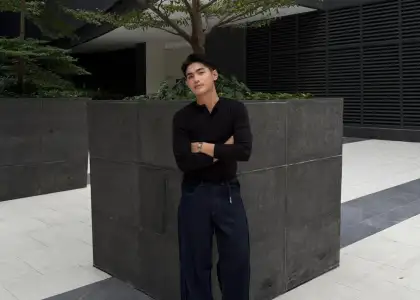 A person in dark clothing leans against a large concrete planter with a tree, set in a modern, minimalist courtyard