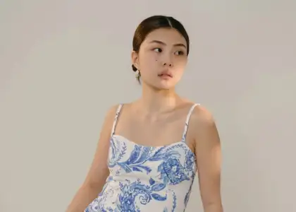 A woman gazes to the side, wearing a white dress with blue floral patterns