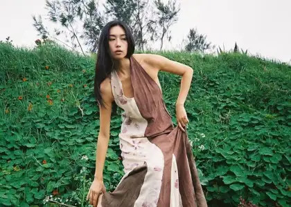 A woman in a flowing, two-tone dress poses thoughtfully on a verdant hillside