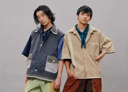 Two young men pose confidently against a gray backdrop