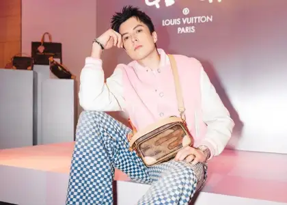 A person wearing a pink varsity jacket and checkered pants in front of a Louis Vuitton signage