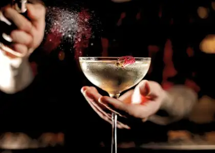 A bartender skillfully pours a colorful cocktail into a glass, showcasing the drink's vibrant hues and textures.