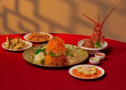 A vibrant and artfully arranged Chinese New Year dish, likely Yusheng, takes center stage on a deep red tablecloth.