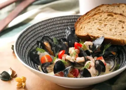 Bowl of creamy mussels with shrimp, cherry tomatoes, and dill garnish, accompanied by slices of rustic bread
