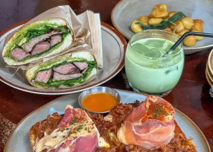 A plate of sliced steak sandwich with lettuce, iced matcha drink, crispy gnocchi, and cured meat-topped dish with sauce
